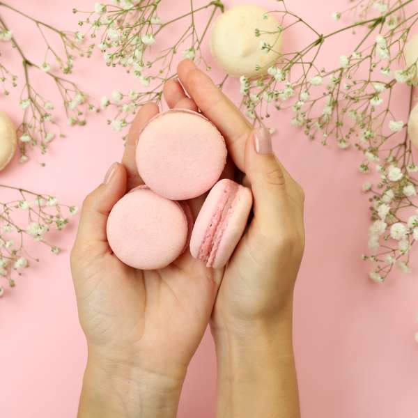 female-hands-hold-macaroons-on-pink-background-with-macaroons-and-flowers.jpg